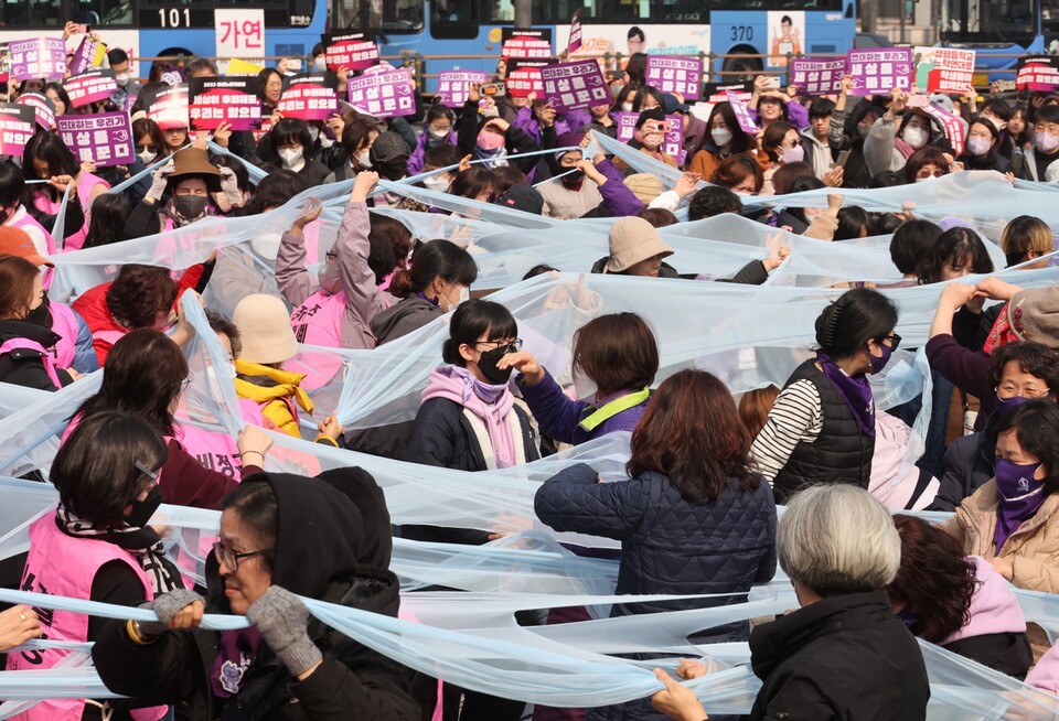 4일 서울 종로구 보신각 앞에서 열린 2023 여성노동자대회. 참가자들이 여성차별의 상징인 유리천장을 깨고 나가자는 의미로 투명한 천을 찢는 퍼포먼스를 하고 있다. (연합뉴스)